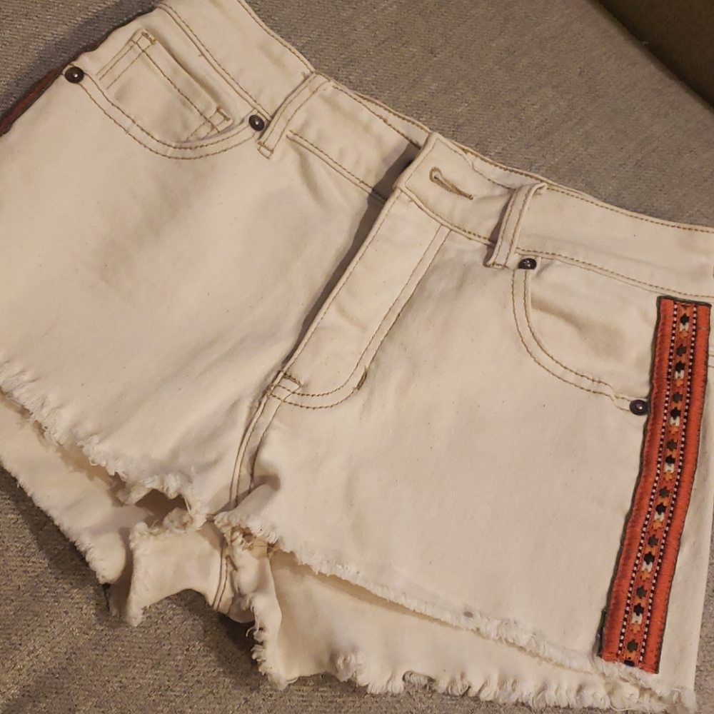 Cream button fly jean shorts with orange detail.